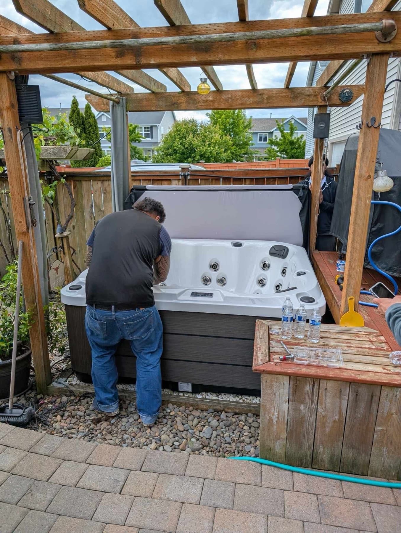 Crew finishing a hot tub install under a pergola on a paver patio