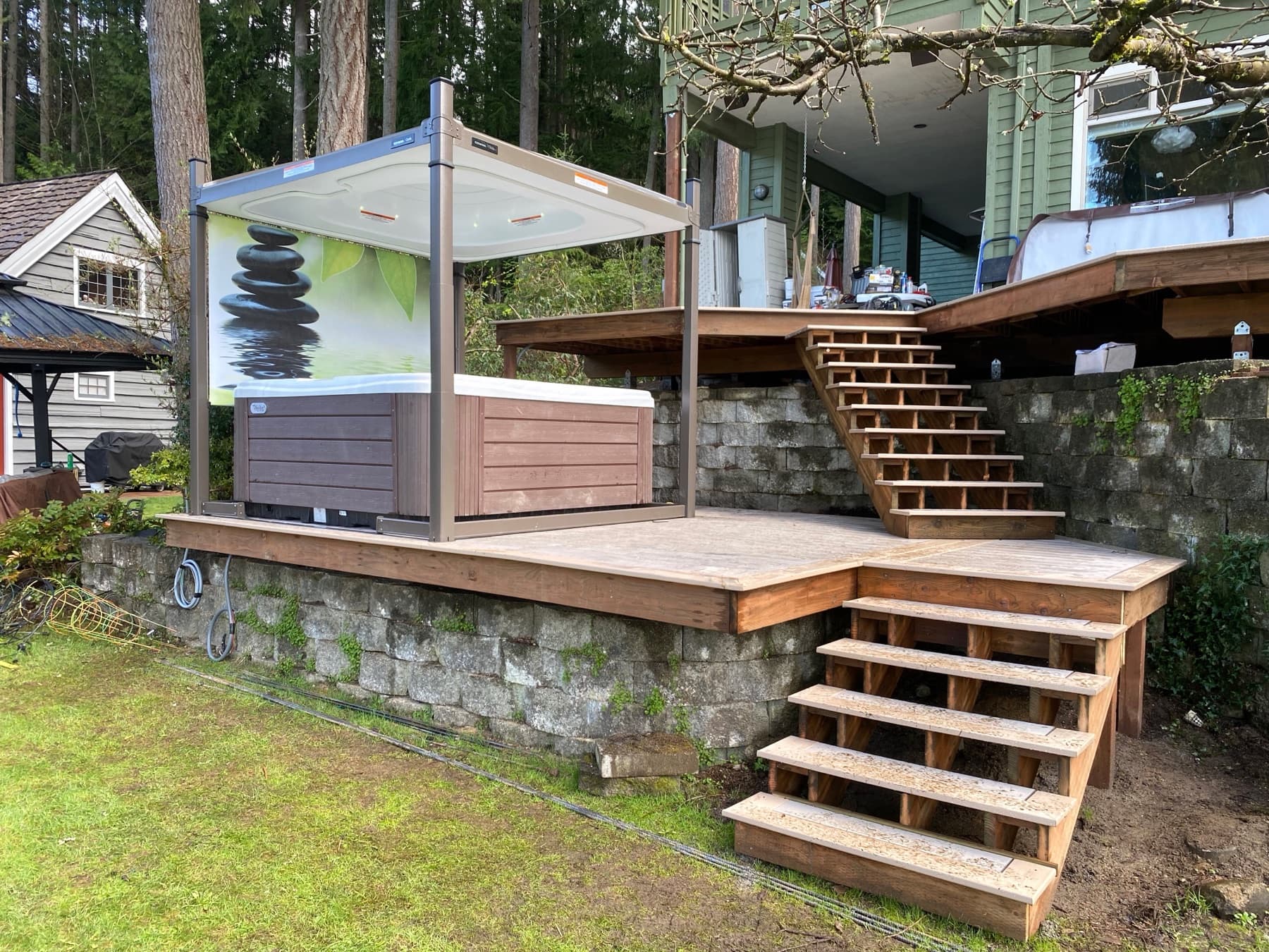 Hot tub under a gazebo beside a raised cedar deck and stone retaining wall