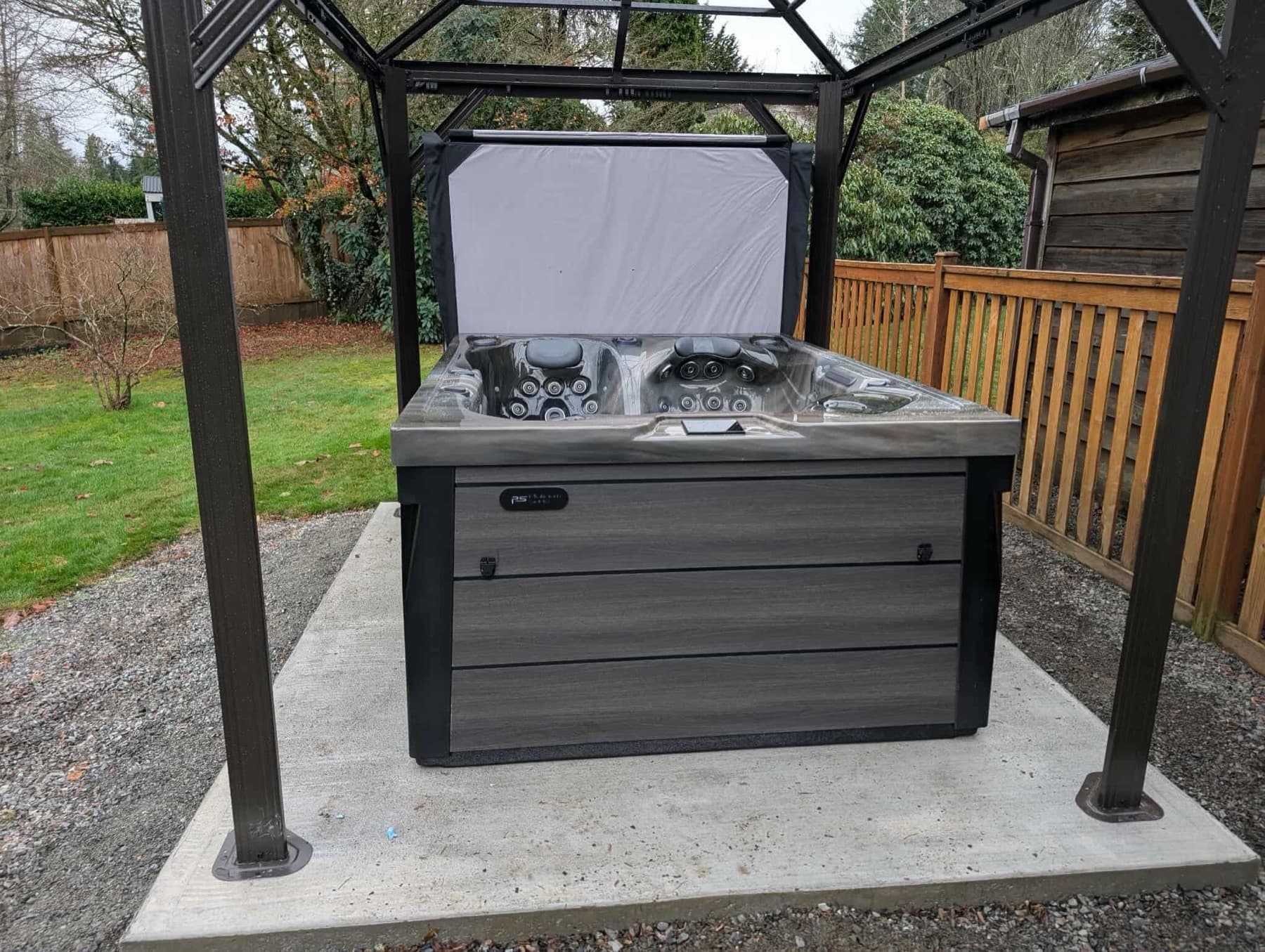 Hot tub under a metal gazebo on a concrete pad in a fenced backyard
