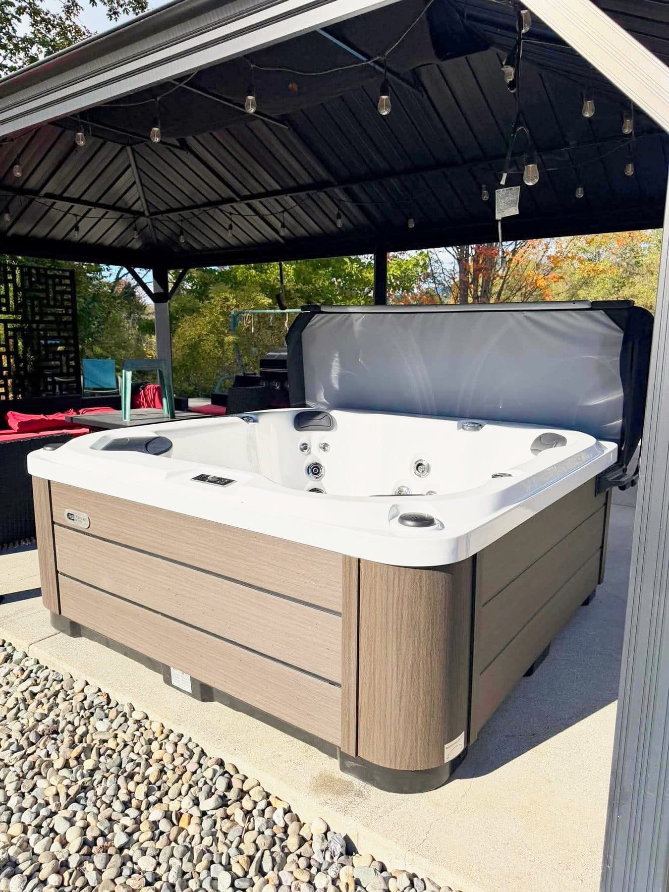 Hot tub under a black gazebo on a gravel pad beside the patio