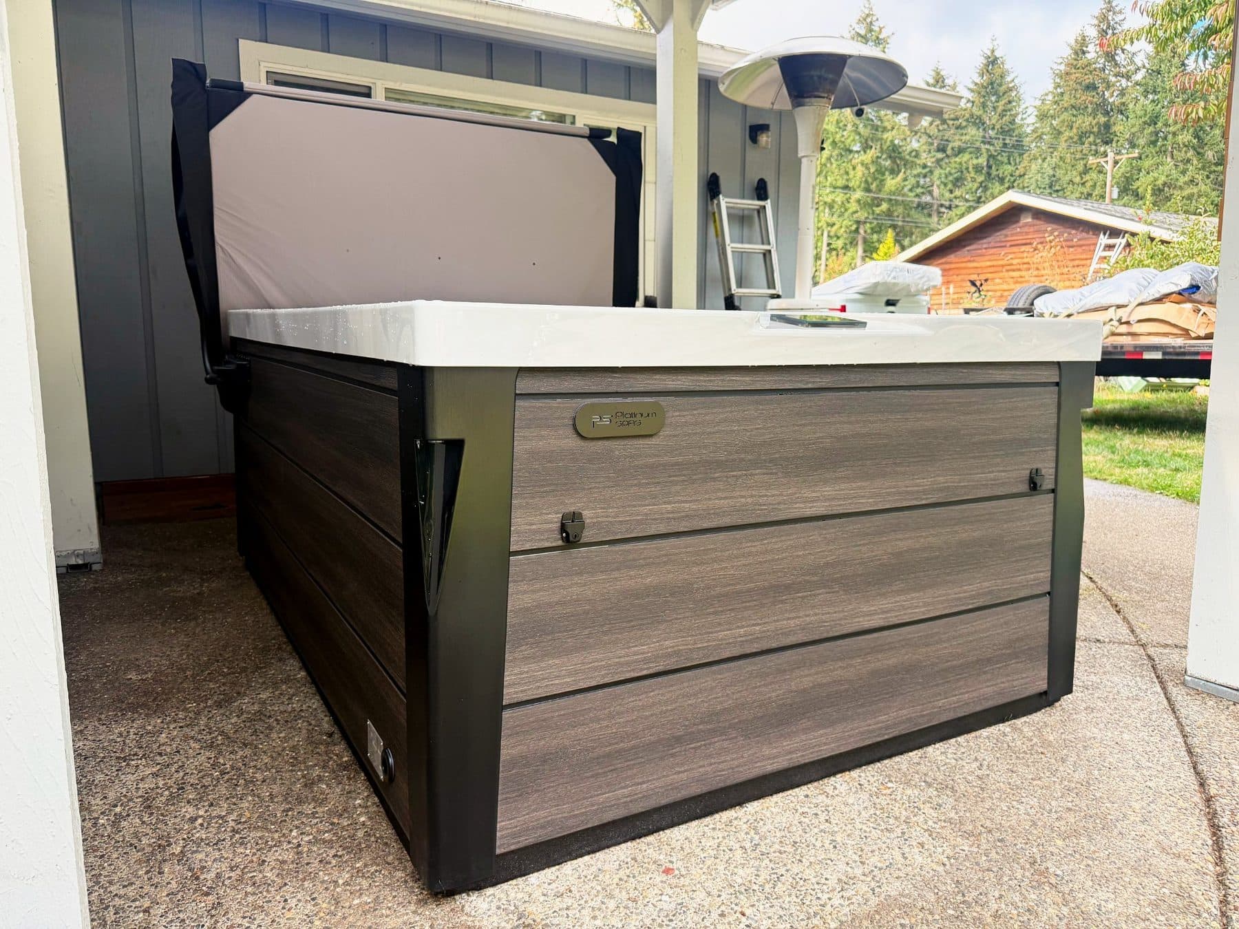 Hot tub with the cover closed on a concrete pad next to the house