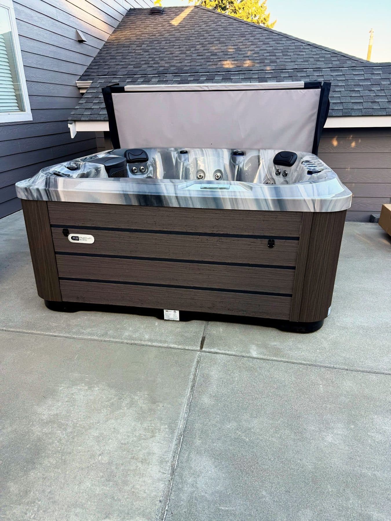 Hot tub with the cover open on a driveway pad beside the garage