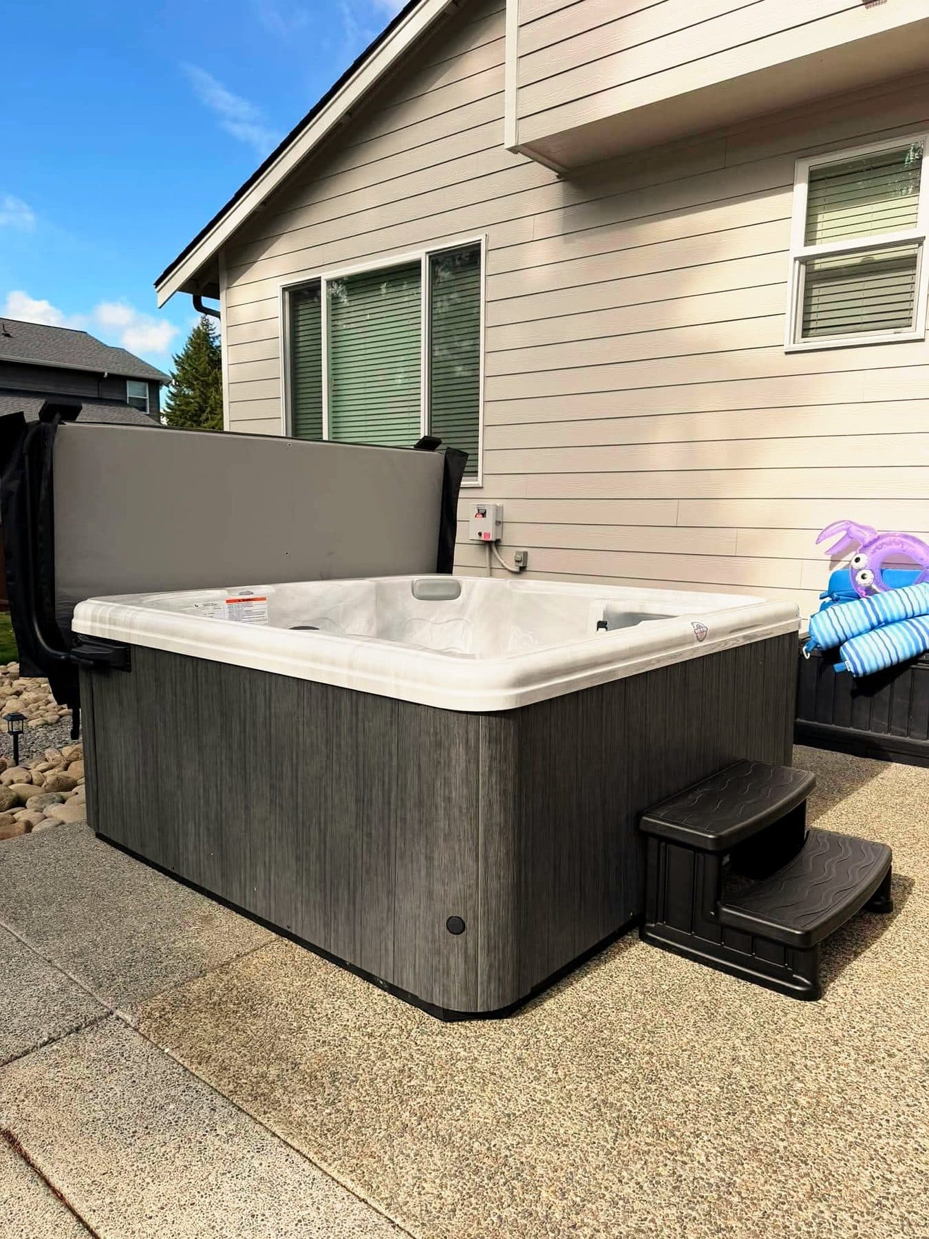 Grey hot tub with steps on a concrete pad under the kitchen window