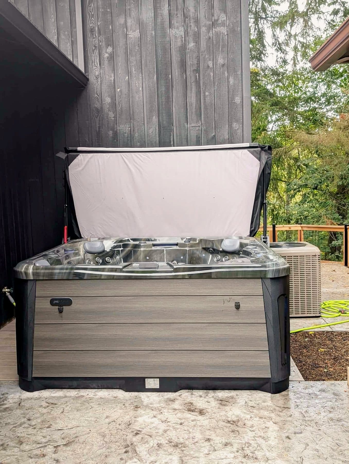 Hot tub with the cover open beside a cedar-sided home
