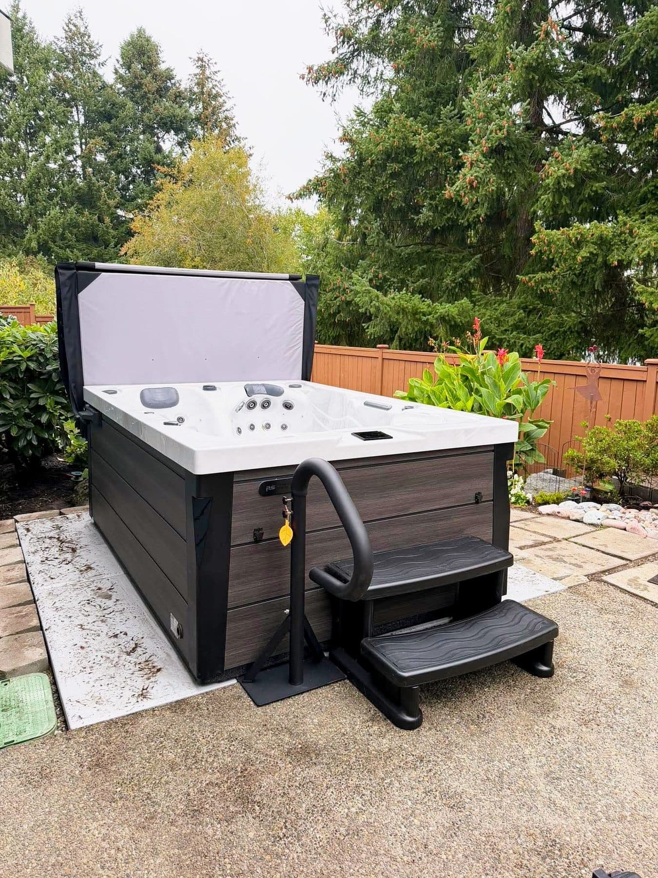 Hot tub with steps and cover lifter in a fenced backyard garden