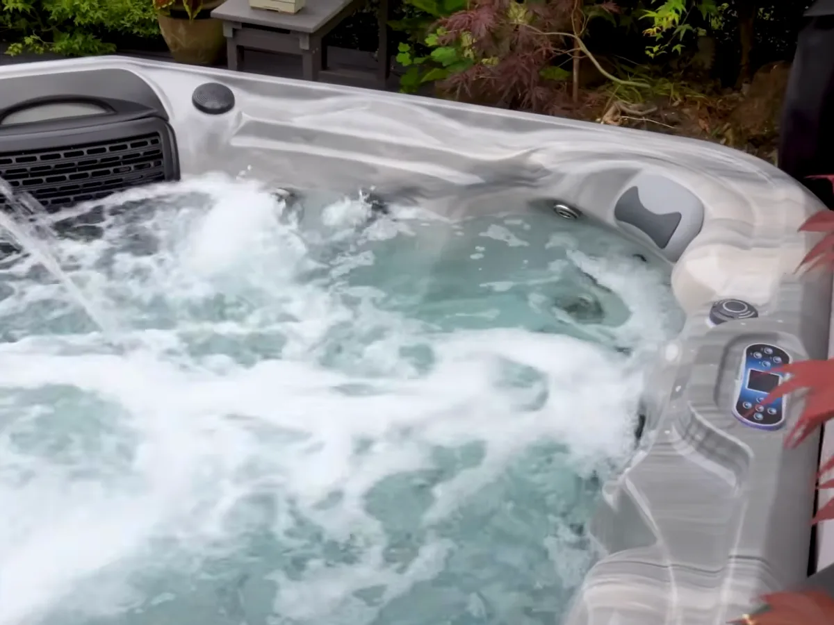 A Platinum Spas Luxury range hot tub with jets running, set in a garden beside a red maple